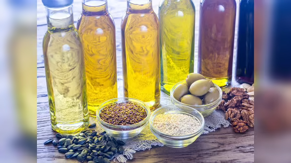 Various cold pressed oils in glass bottles with seeds and nuts on wooden surface